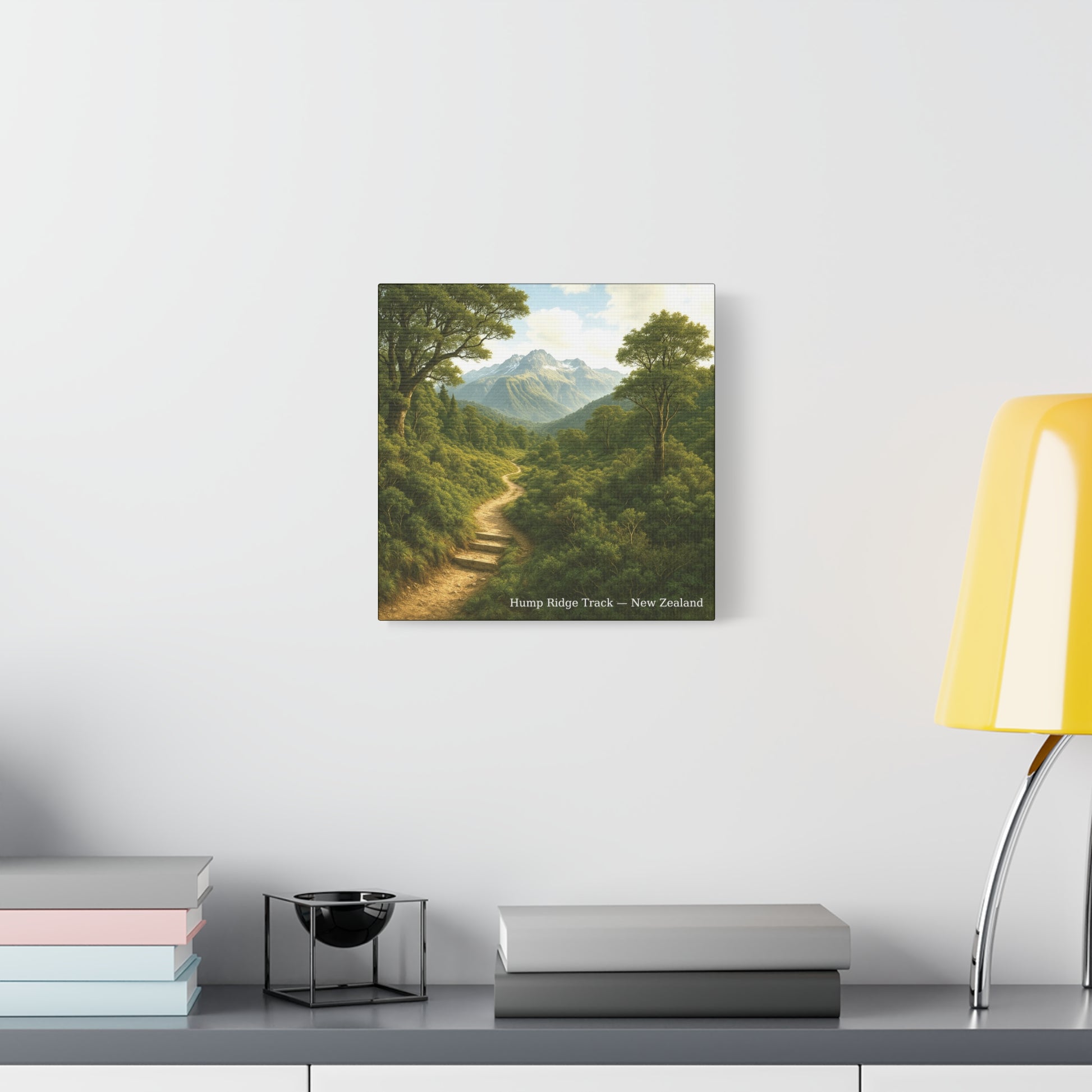 Framed print of a Hump Ridge Track mountain landscape on a wall above a desk with books and a lamp.
