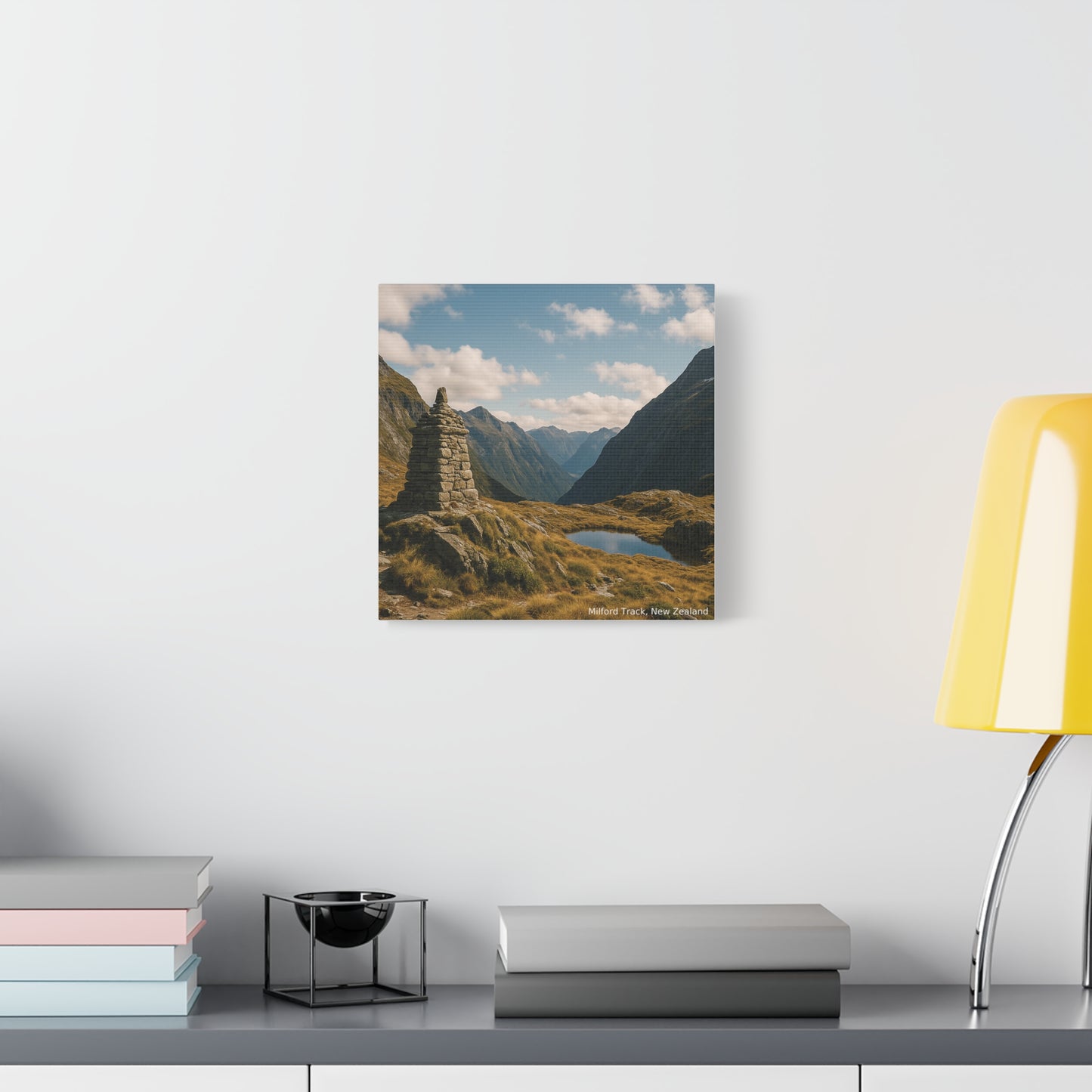 Mountain landscape print on a wall above a desk with books and a lamp.