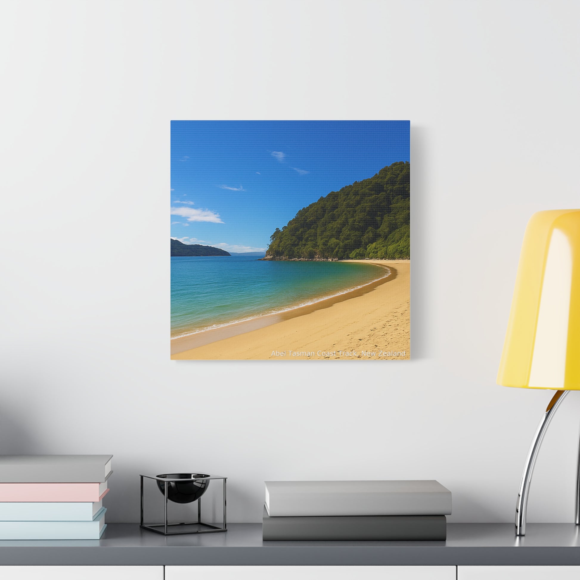 Abel Tasman Canvas print of a beach scene on a wall above a desk with books and a lamp.