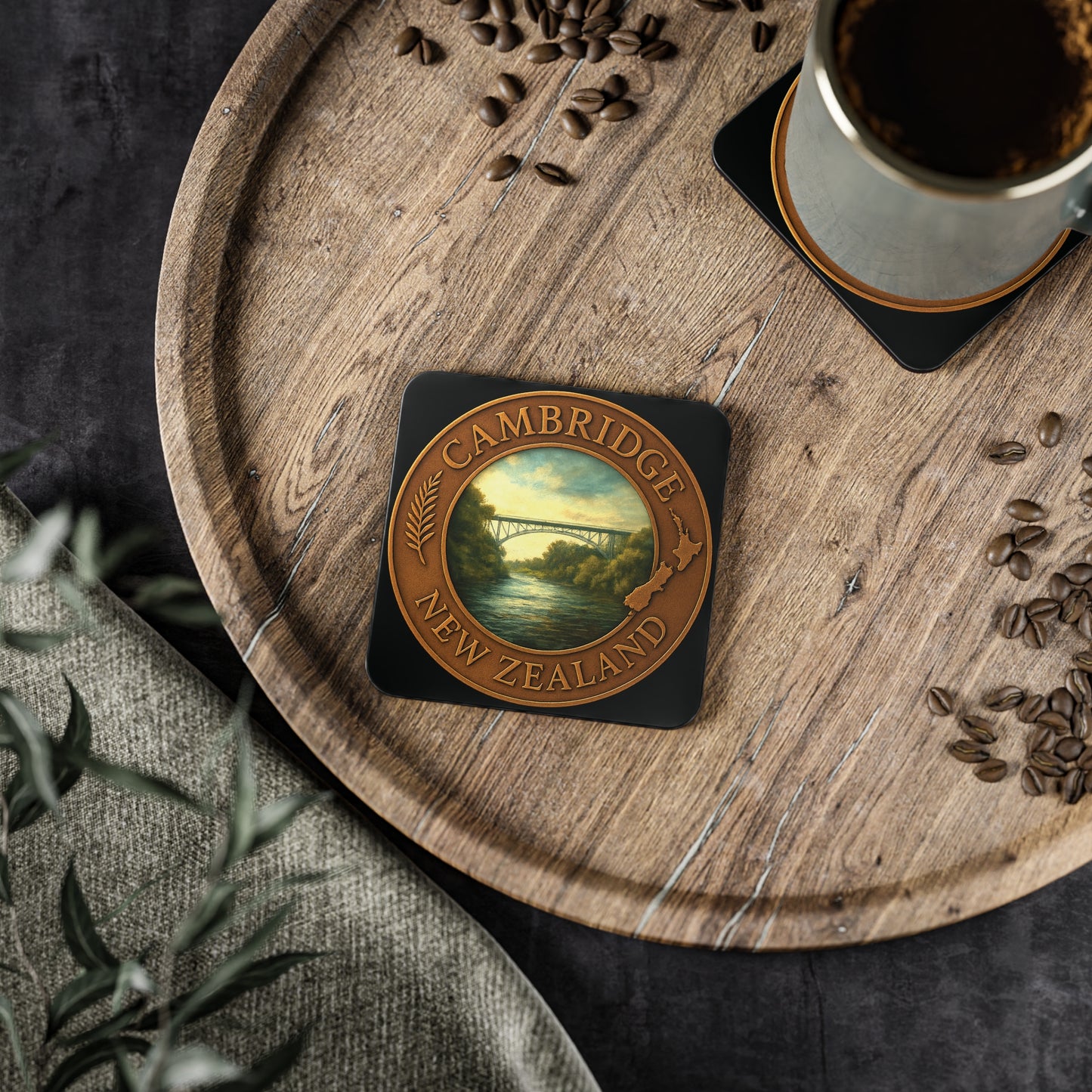 Coaster with 'Cambridge New Zealand' design on a wooden tray with coffee and coffee beans.