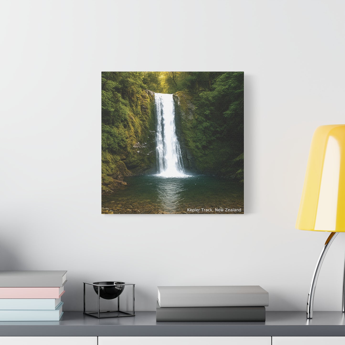 Framed photograph of a Kepler Track waterfall in a forest on a wall above a desk with books and a lamp.