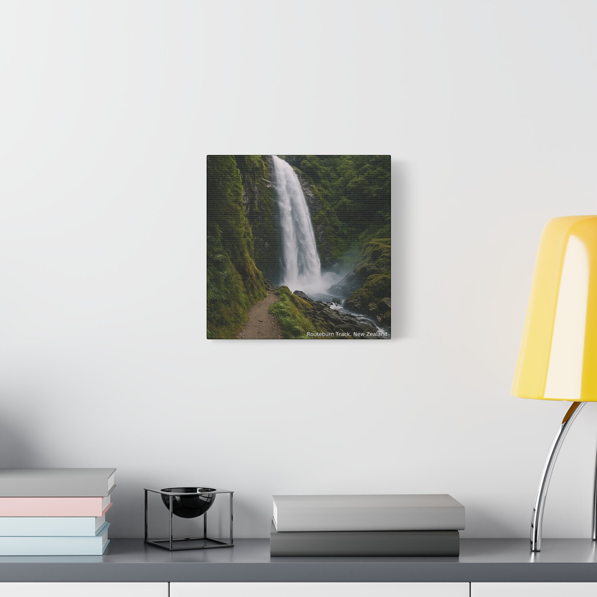 Routeburn Track Framed photograph of a waterfall on a wall above a desk with books and a lamp.