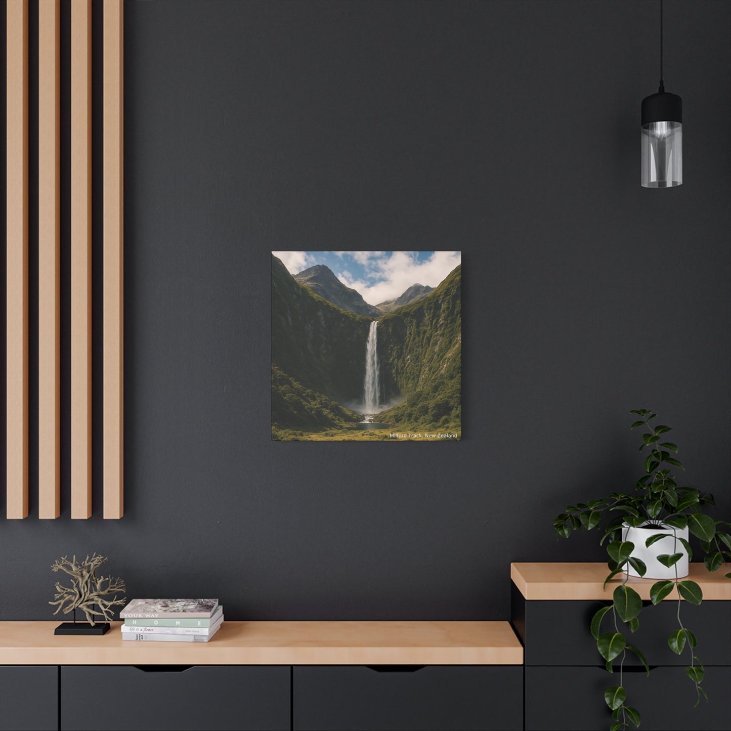 Framed landscape print of a Milford Track waterfall on a dark wall with wooden shelves and decor.