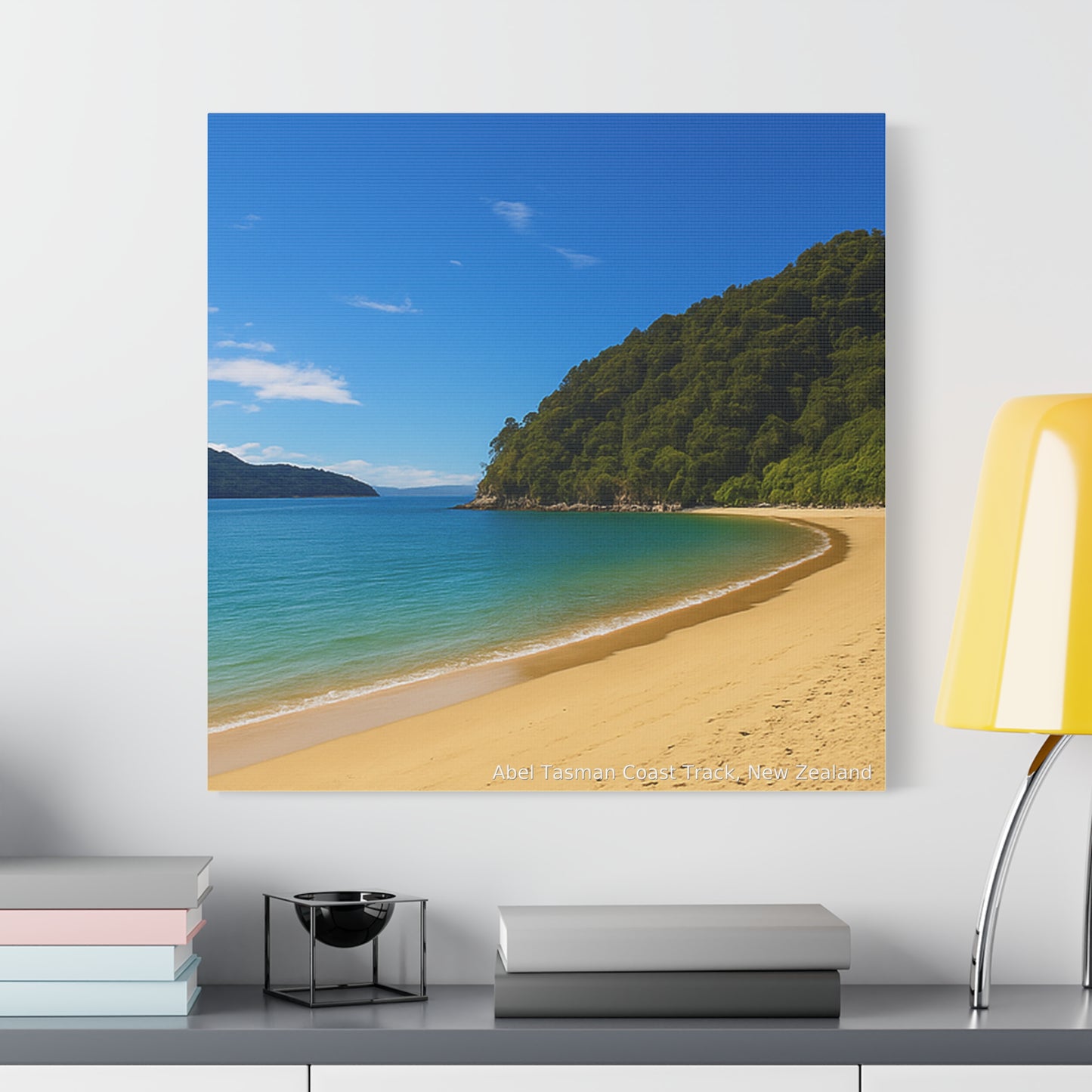 Abel Tasman Beach scene with clear blue sky and green mountains on a wall above a shelf.