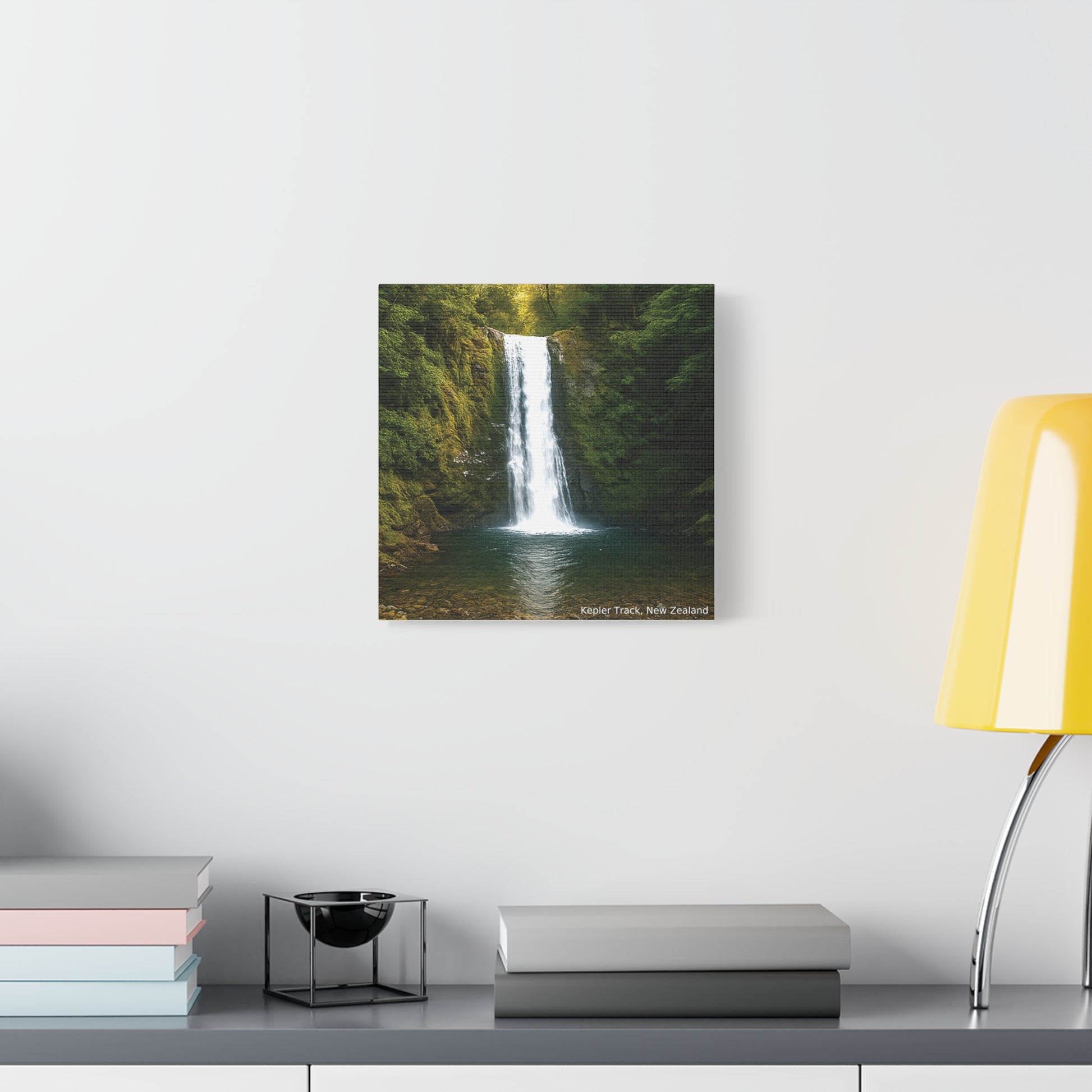 Framed photograph of a waterfall on a wall above a desk with books and a lamp.