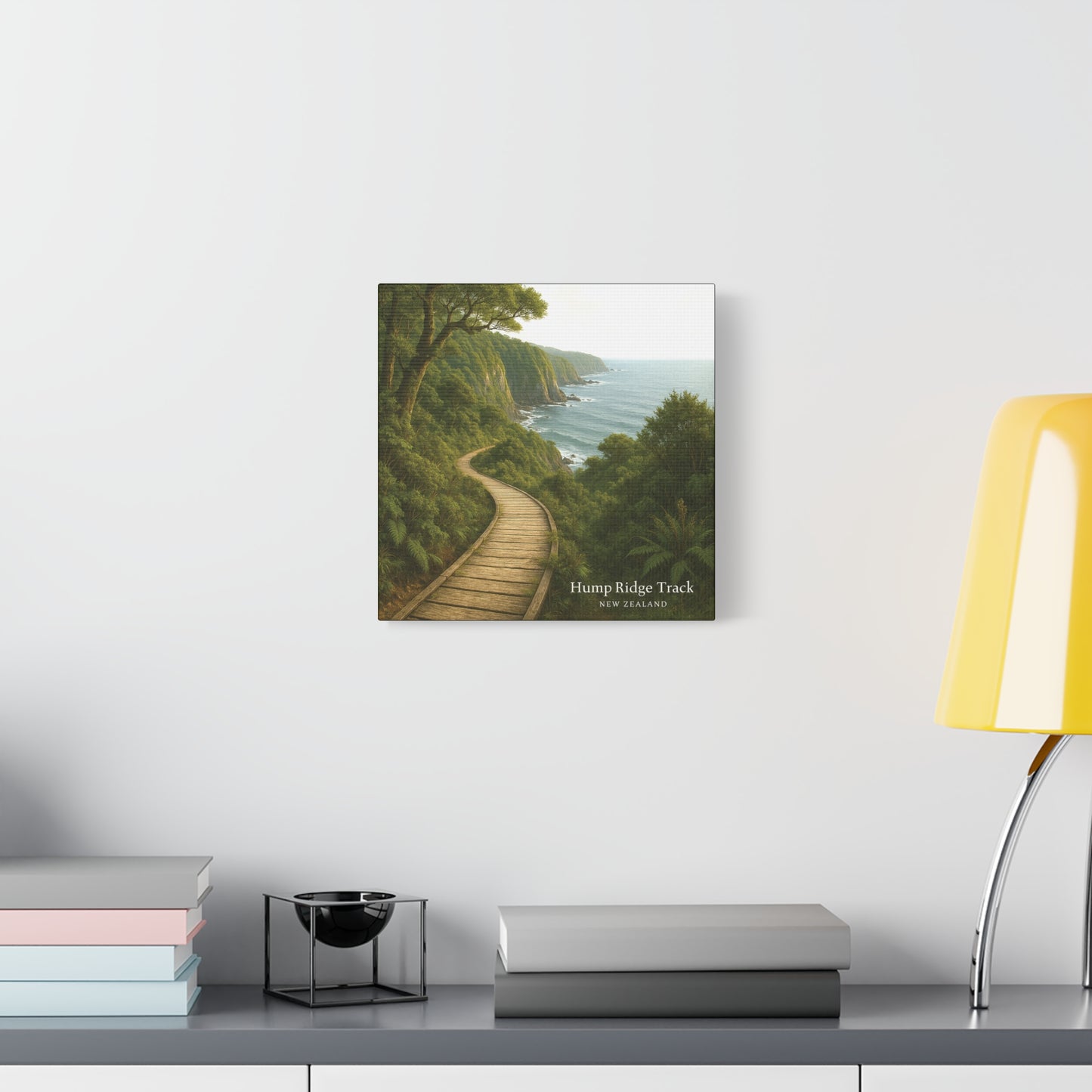Hump Ridge Track Framed artwork of a coastal path with trees on a white wall above a desk.