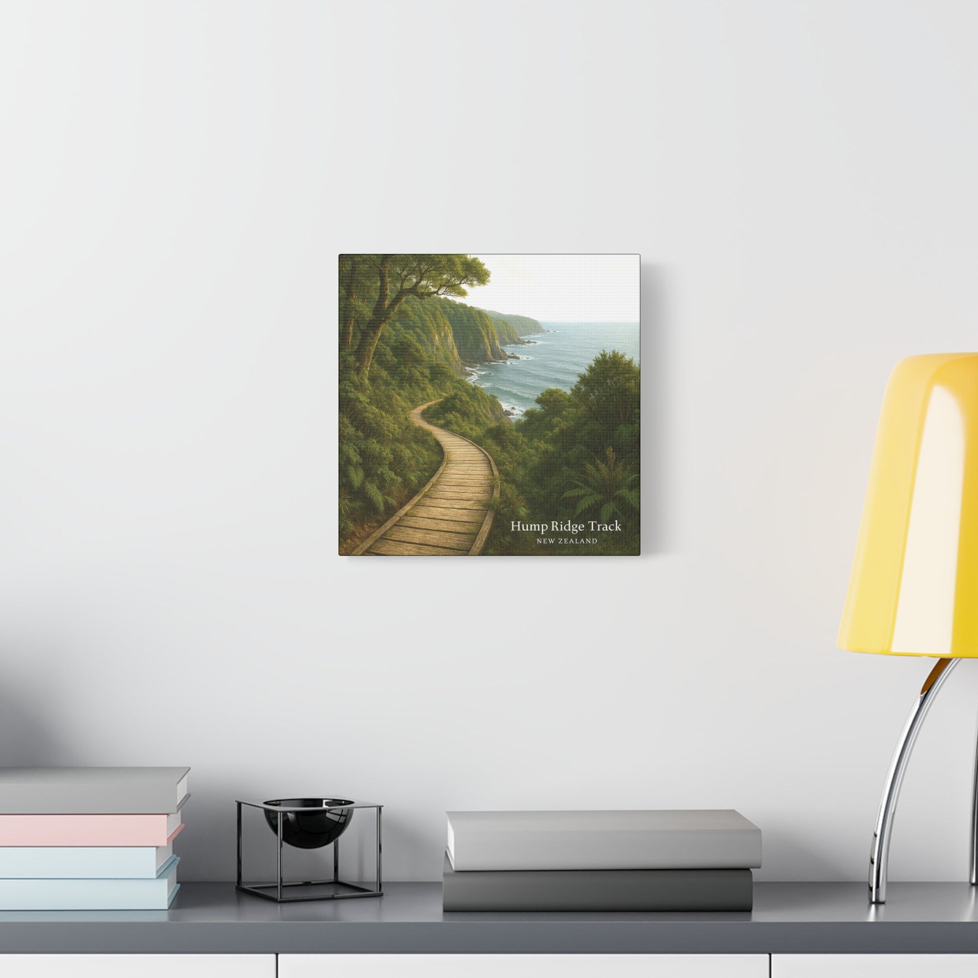 Hump Ridge Track Framed artwork of a coastal path with trees on a white wall above a desk.